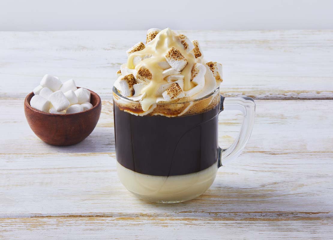 Taza de cristal de café bombón coronado con crema chantillí, masmelos y leche condensada