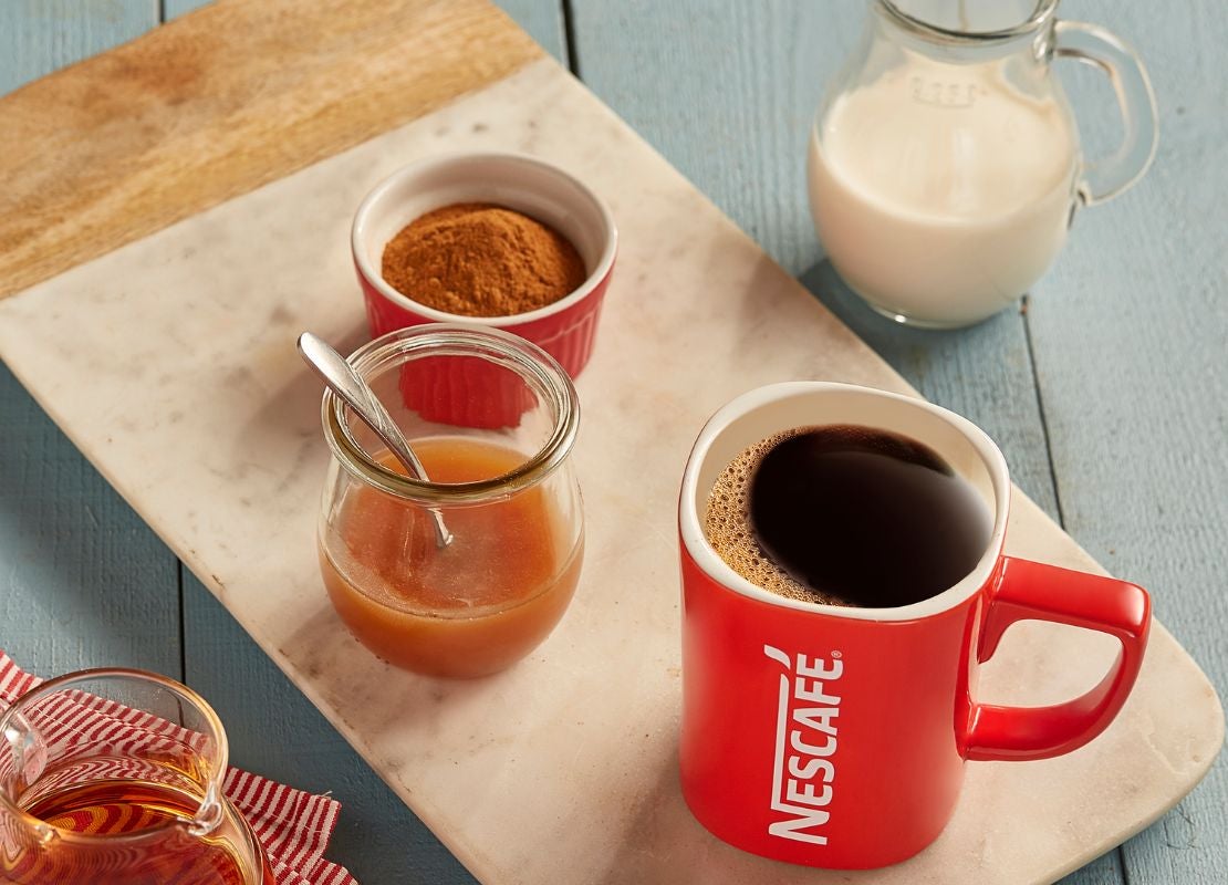 Taza de café negro preparada con café soluble, acompañada de leche, miel y especias.