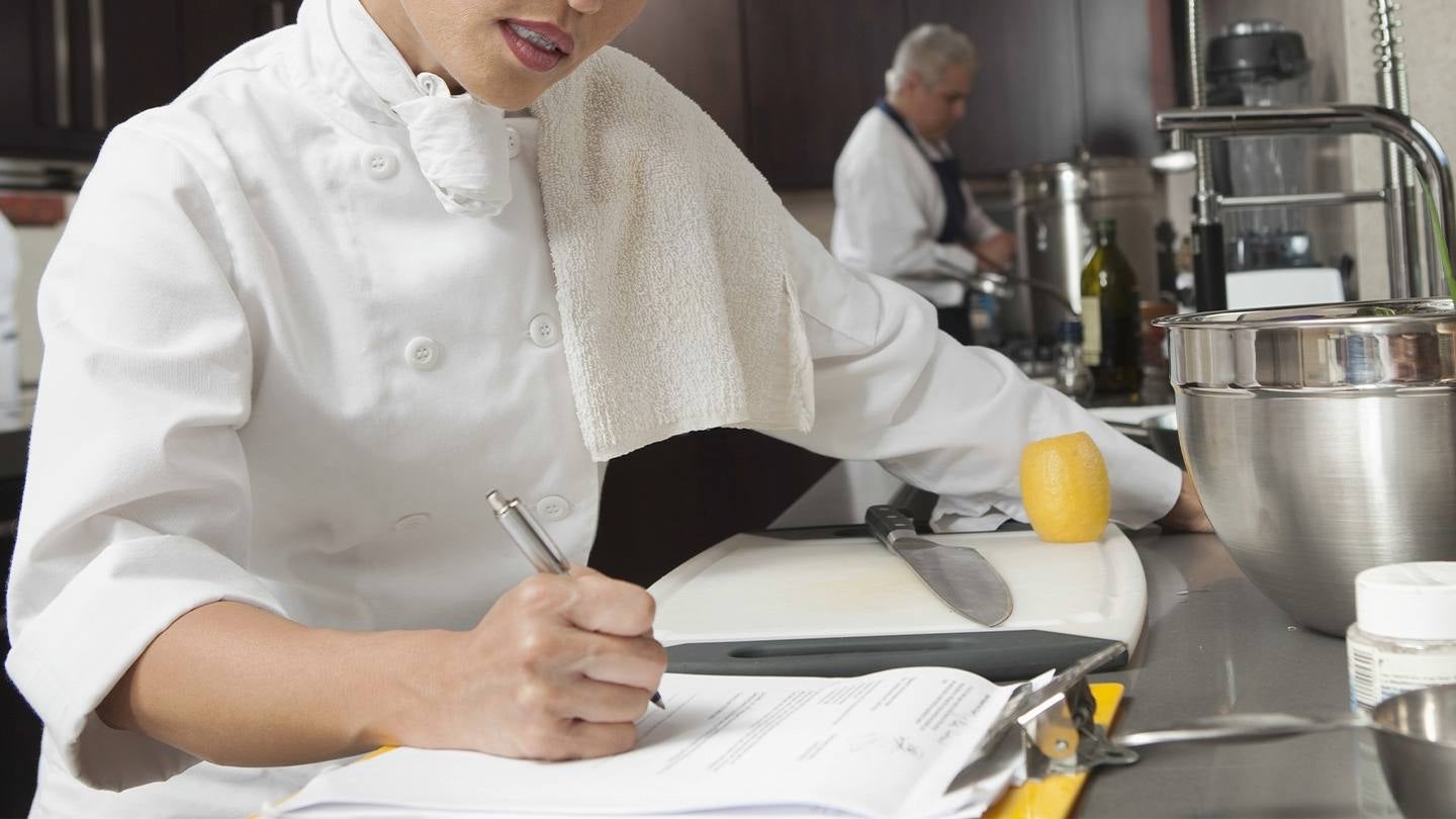 Chef revisa documentos en cocina profesional para identificar cuellos de botella en la operación.