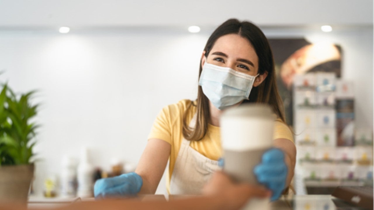 Trabajadora con mascarilla entrega una bebida como parte del servicio de alimentos en hospitales.