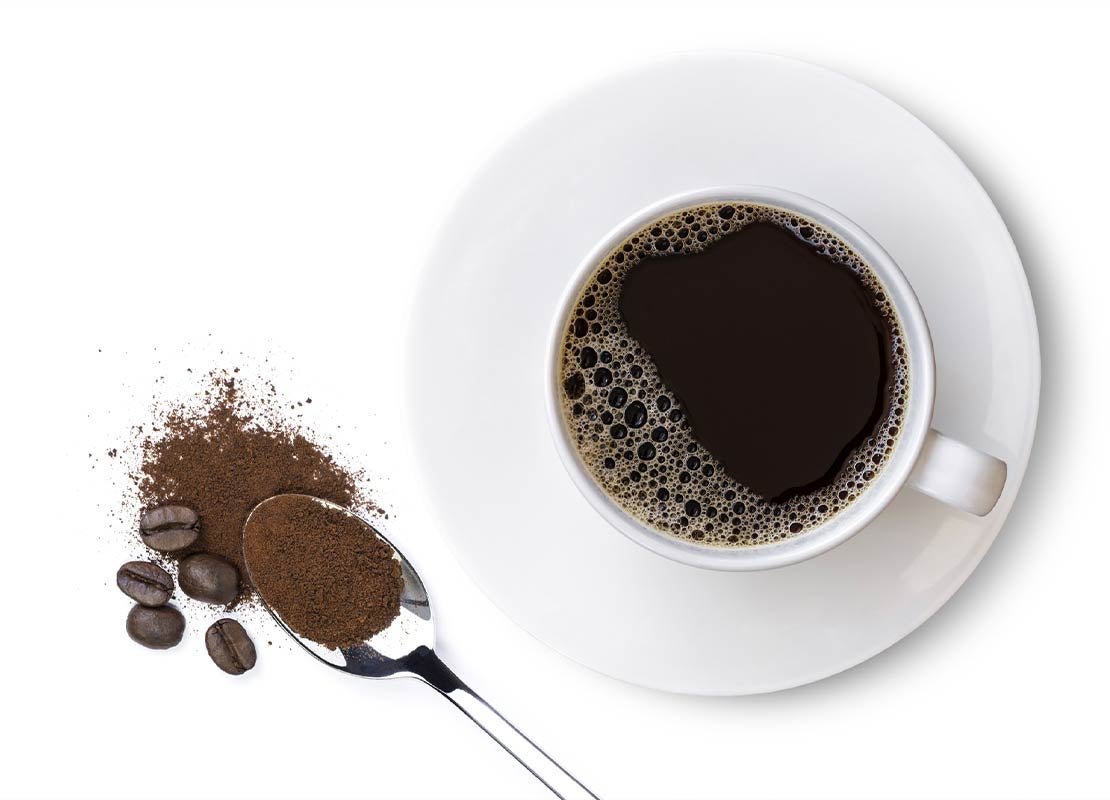 Taza blanca de café americano sobre un plato, cuchara con café soluble y en granos tostados