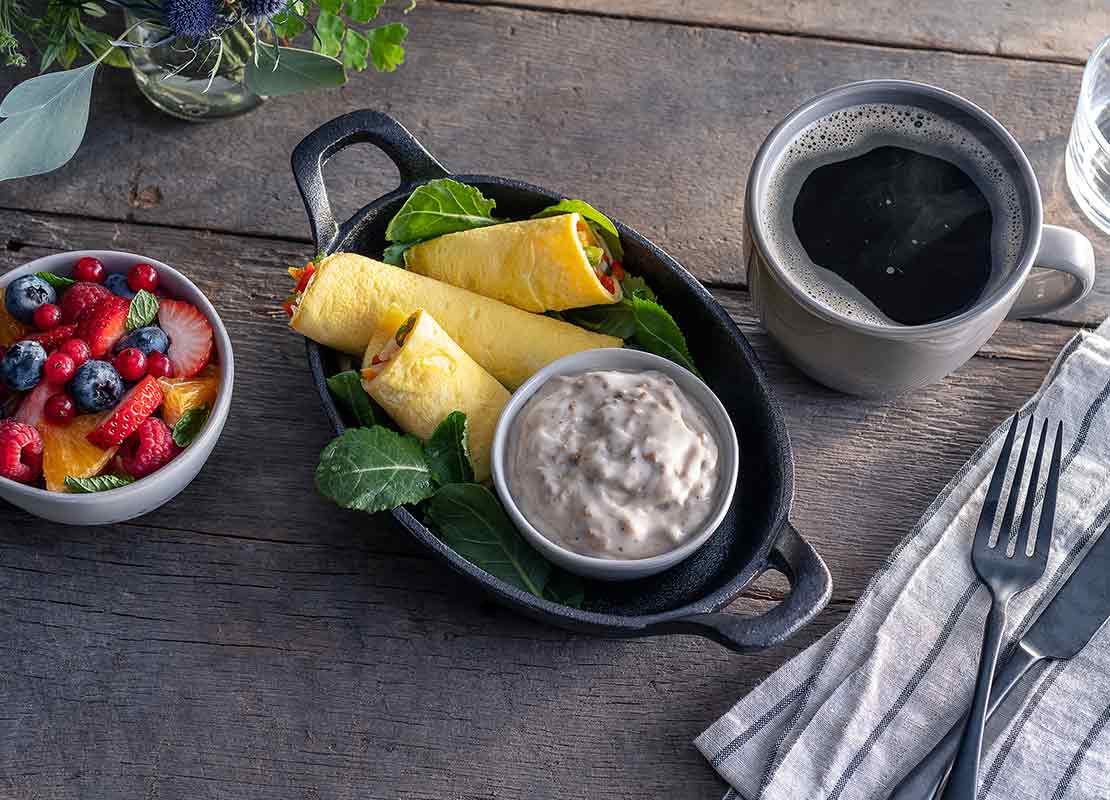 Bandeja negra con wraps, salsa, acompañada de un café soluble y un tazón de fruta fresca