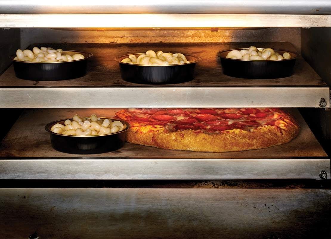 Bandejas con pasta y una pizza cocinándose en horno industrial de doble nivel