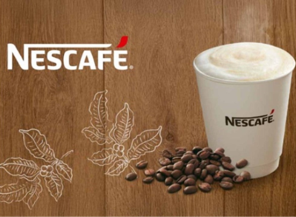 Vaso blanco de cappuccino NESCAFÉ® rodeado de granos de café y con el logo en la esquina