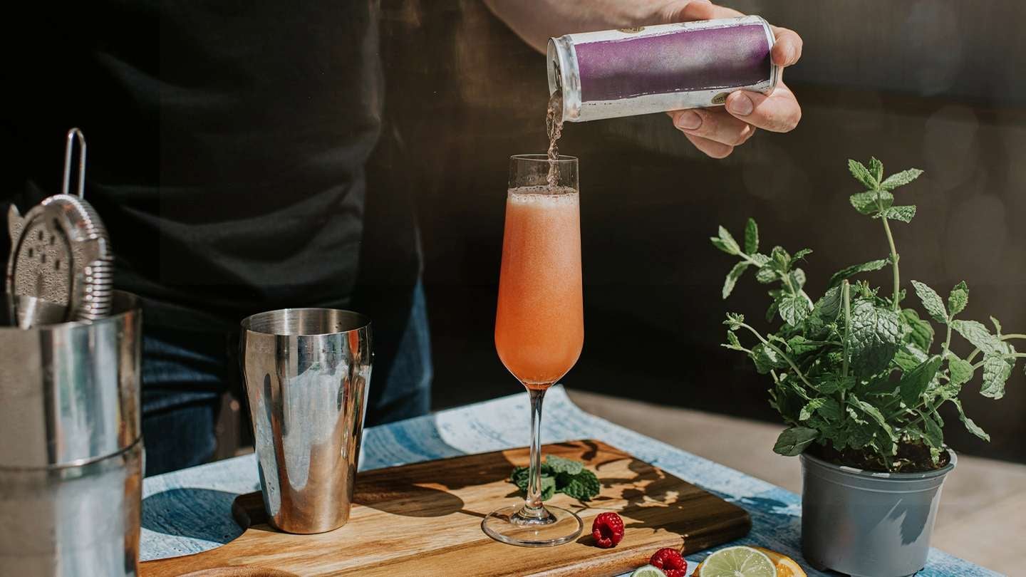 Persona sirviendo una bebida artesanal en copa alargada, decorada con menta, cítricos y frutos rojos