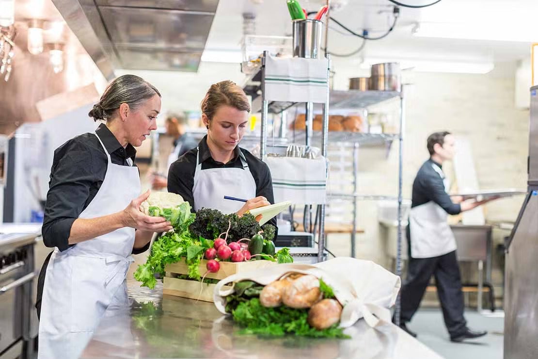 Dos chefs en la cocina de un restaurante revisan alimentos para almacenarlos