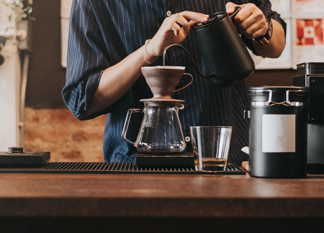 Barista preparando café filtrado con método de goteo manual con V60 y jarra de goteo