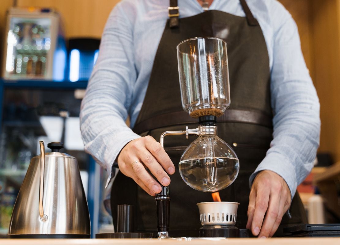 Barista elabora café filtrado con método sifón resaltando precisión y control en la extracción.