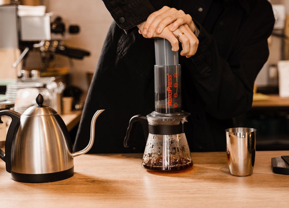 Barista preparando café filtrado con método por presión leve con AeroPress en la barra de una cafetería