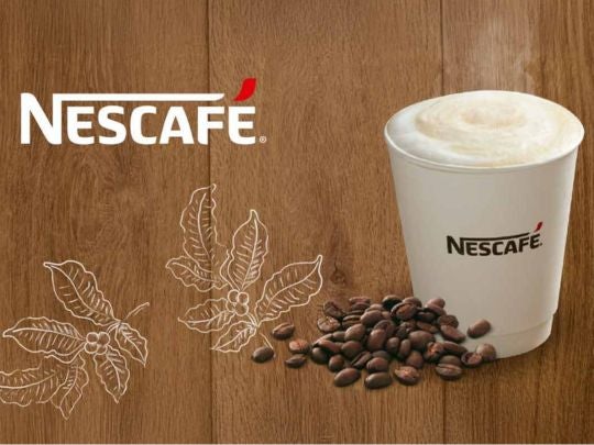 Vaso blanco de cappuccino NESCAFÉ® rodeado de granos de café y con el logo en la esquina