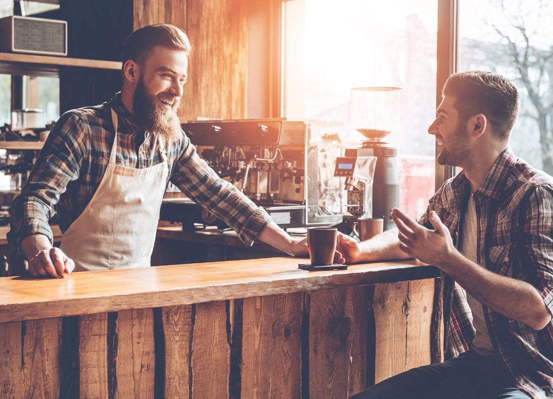 Barista atendiendo cliente en barra de café compacta con maquinaria y espacio optimizado