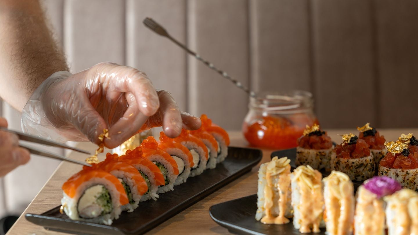 Chef decora sushi con oro comestible para elevar la presentación en cocina profesional.