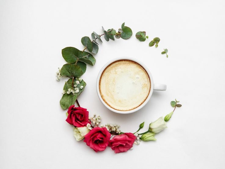 Taza de café preparada con bebida vegetal y rodeada de flores y hojas naturales