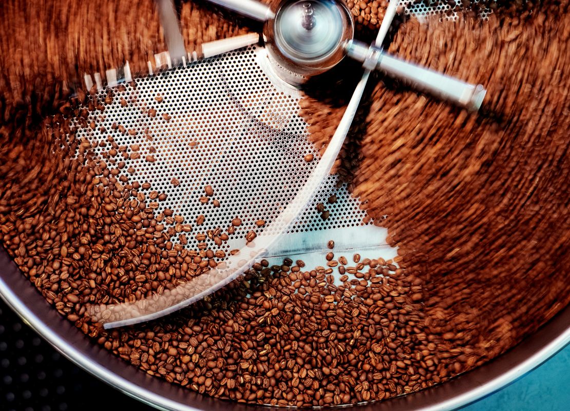 Tostadora industrial mezclando granos de café en movimiento durante proceso de tostado uniforme