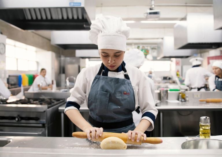 Estudiante de cocina del Programa YOCUTA preparando masa con rodillo en cocina profesional