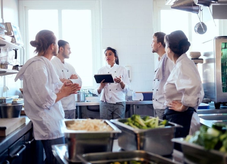 Equipo de cocina escuchando a chef con tablet durante reunión en cocina