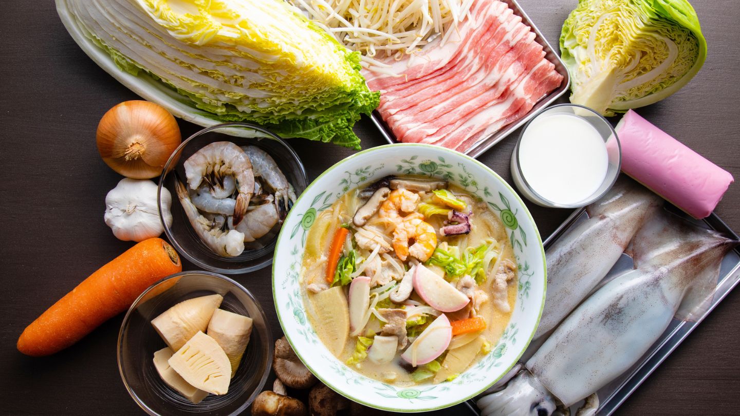 Vegetales, mariscos y carne frescos dispuestos alrededor de un plato con champon de Nagasaki