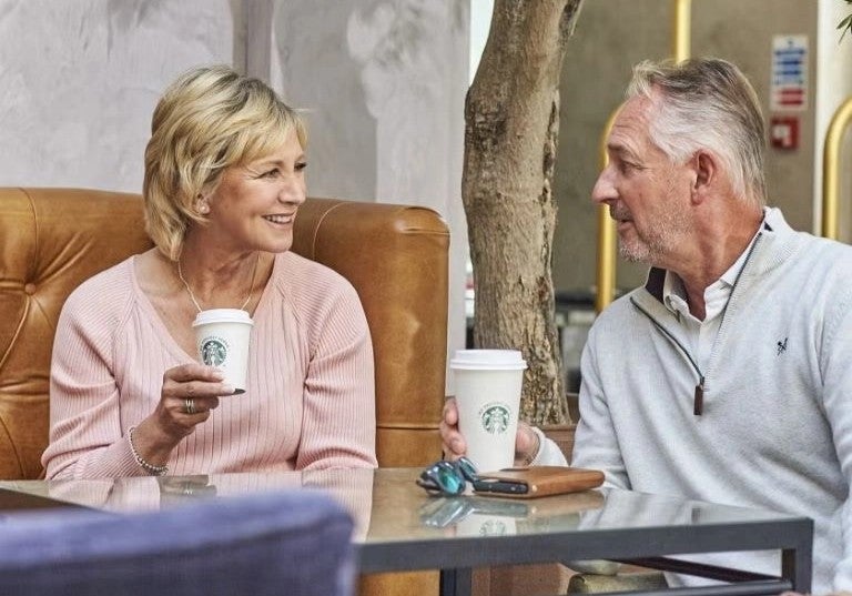 Pareja de adultos mayores conversando en lounge de hotel mientras disfrutan café caliente.