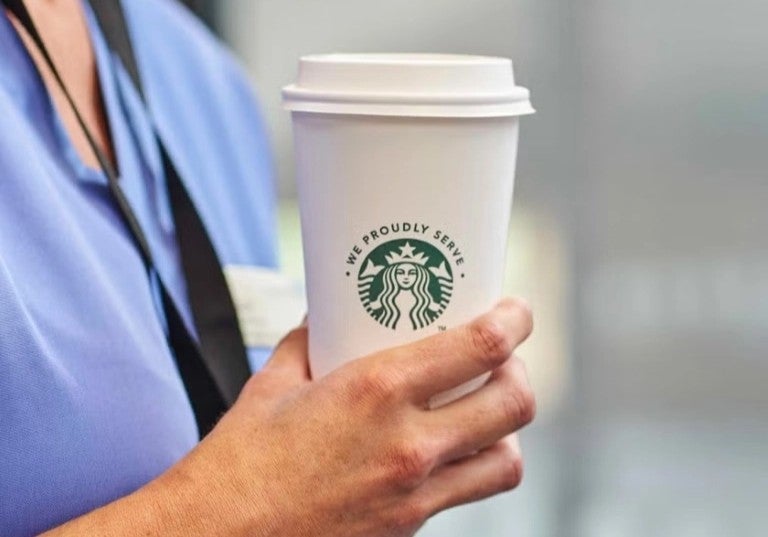 Profesional de la salud sosteniendo vaso de café para llevar en un entorno clínico.