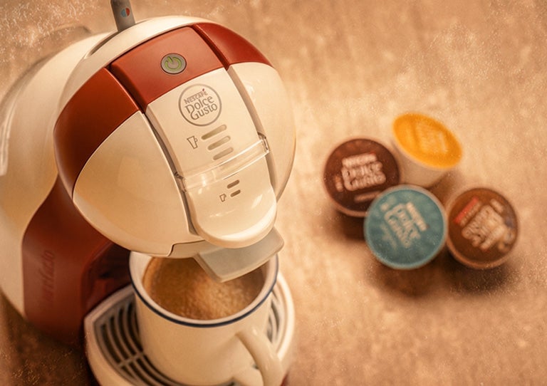 Máquina NESCAFÉ® Dolce Gusto® preparando bebida con cápsulas de colores al lado
