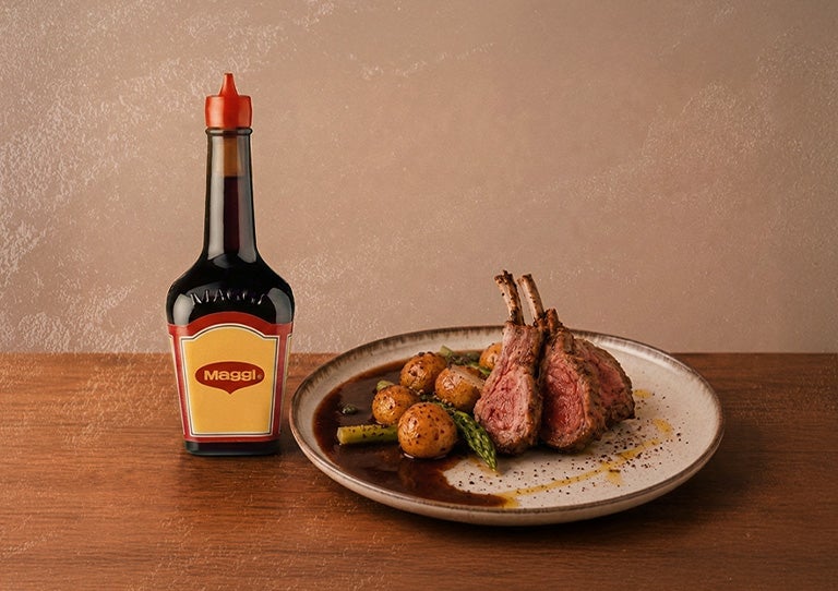 Botella de sazonador MAGGI® junto a un plato con carne y papas con salsa servidos en la mesa