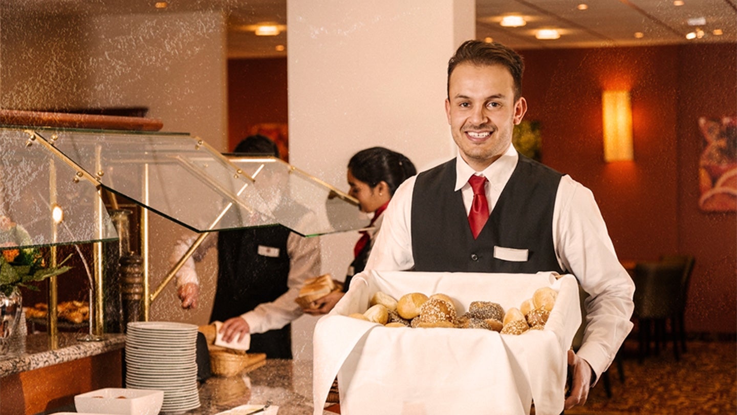 Mesero sostiene una caja con panes para surtir el buffet de un hotel