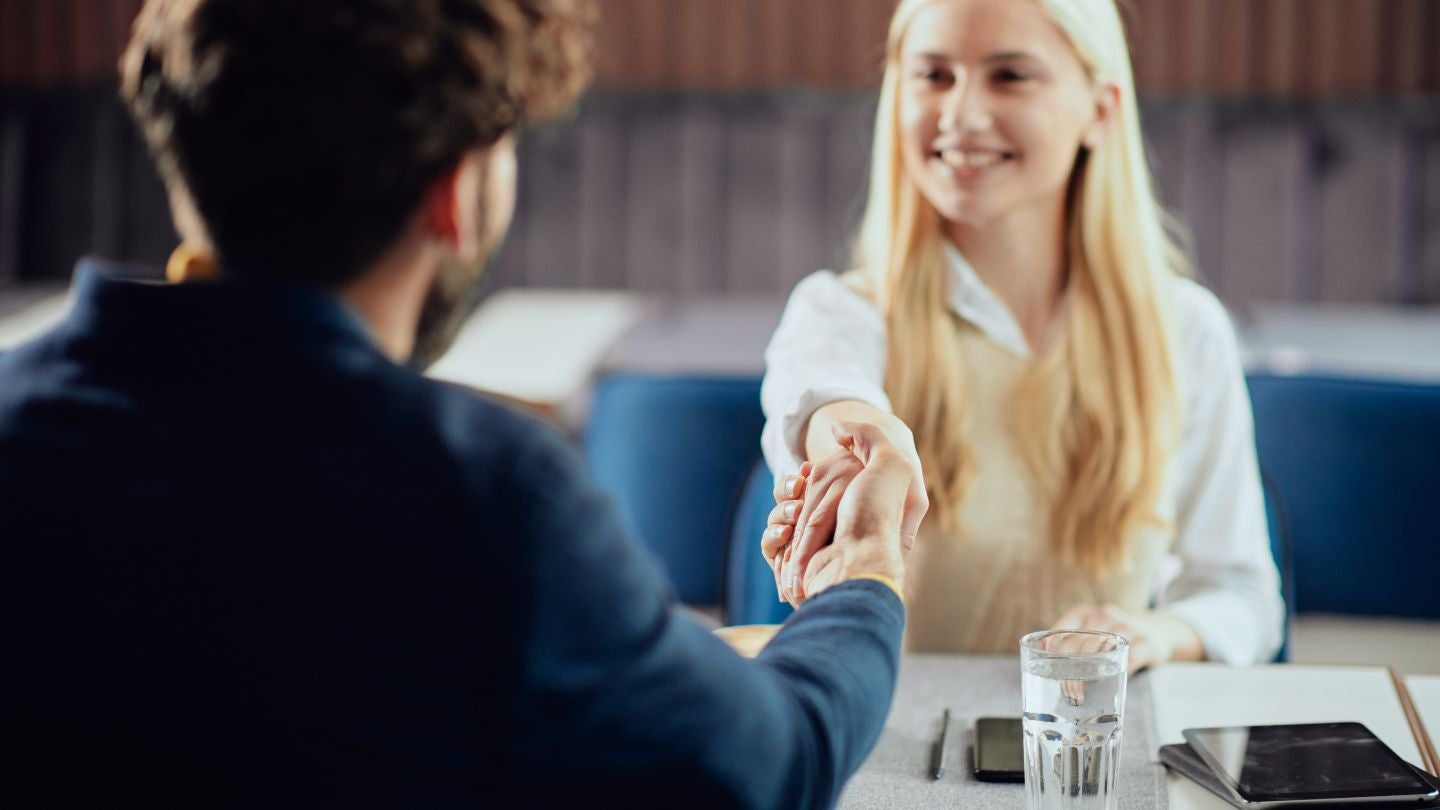 Dos personas se dan la mano sobre una mesa con vaso de agua y teléfono