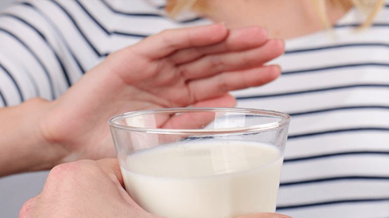 Mano de mujer rechaza vaso de leche porque es intolerante a la lactosa  