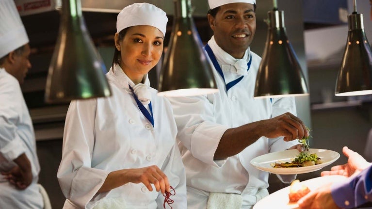 En el Día Internacional del Chef, cocineros vestidos de blanco en una cocina industrial decoran platos de comida