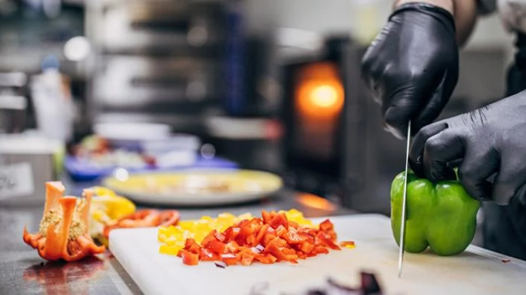 Un chef está cortando un pimiento morrón verde en una tabla de cortar en una cocina