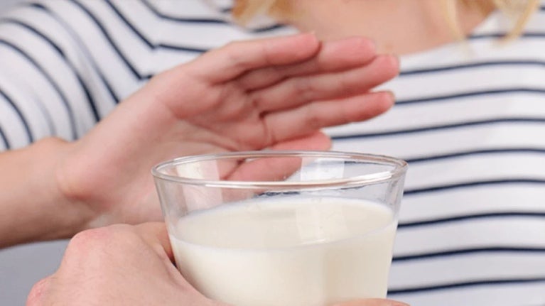 Mano de mujer rechaza vaso de leche porque es intolerante a la lactosa 