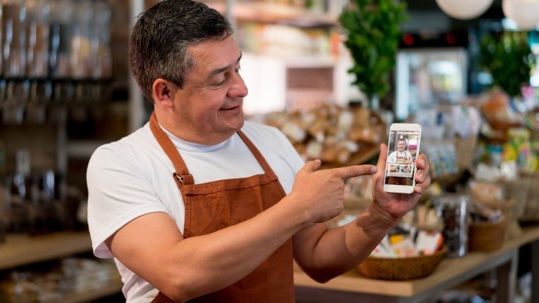 Barista en su negocio muestra en un smartphone el video creado para potenciar su plan de marketing gastronómico