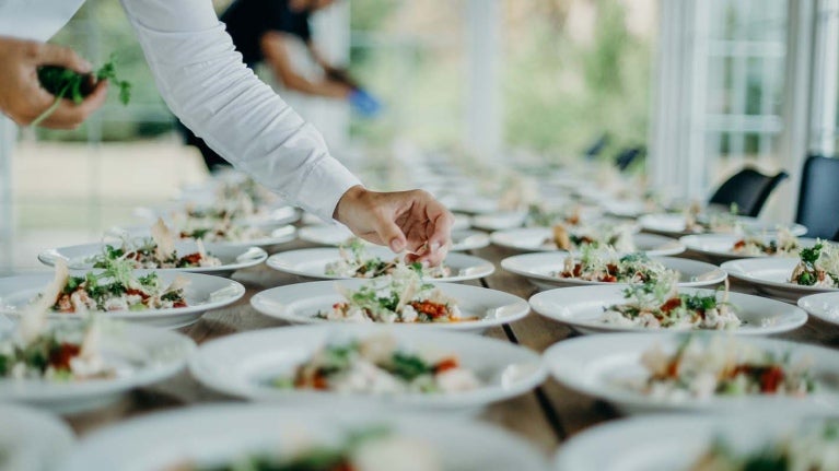 Personal capacitado sirve y decora varios platos ubicados ordenadamente en una mesa para un servicio de catering