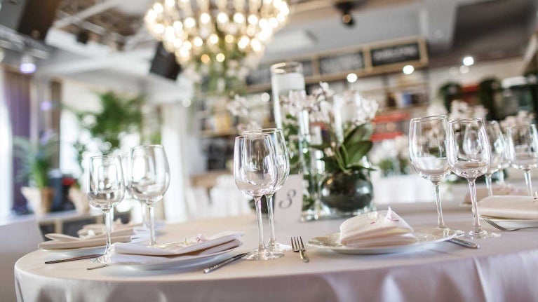 Juego de mesa con copas, platos blancos y lámparas de araña de luz en el fondo que aportan a la decoración de restaurantes