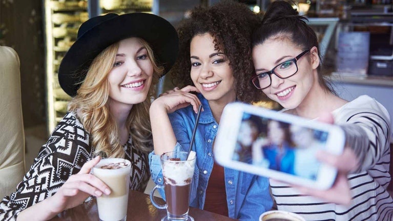 Tres influencers gastronómicas en una cafetería se toman fotos para crear contenido mientras disfrutan de diversas bebidas