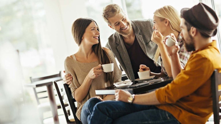 Grupo de Millennials reunidos alrededor de una mesa mientras comparten una taza de café