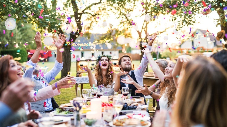 Recién casados y sus invitados vitorean mientras están sentados a la mesa al aire libre con platillos servidos como picnic