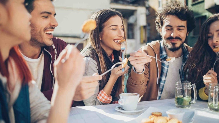 Cinco comensales emocionados disfrutan al aire libre algunos bocadillos y bebidas en la mesa de un restaurante