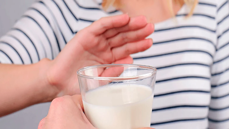 Mano de mujer rechaza vaso de leche porque es intolerante a la lactosa