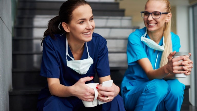 Profesionales de la salud sentados en una escalera, tomando un café con una amplia sonrisa
