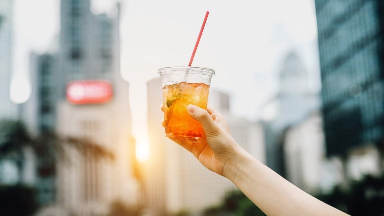 La mano de una persona en la calle sosteniendo un té frío y de fondo una ciudad