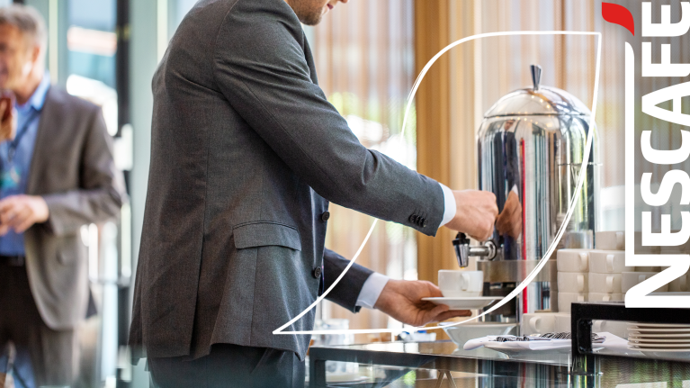 Hombre sirviendo café en un ambiente de hotel, con una taza en la mano.