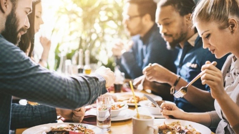 Un grupo de personas disfrutando de una comida juntos en un restaurante, con platos de comida y bebidas en la mesa.