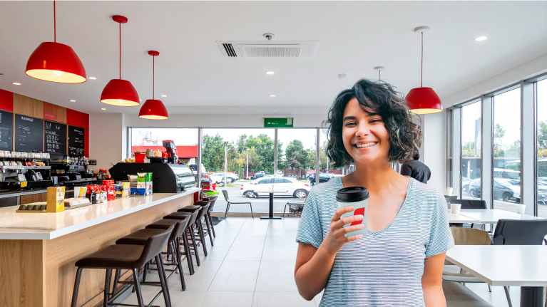 Mujer sonriendo con vaso de café en la mano en un tienda en una estación de servicio.
