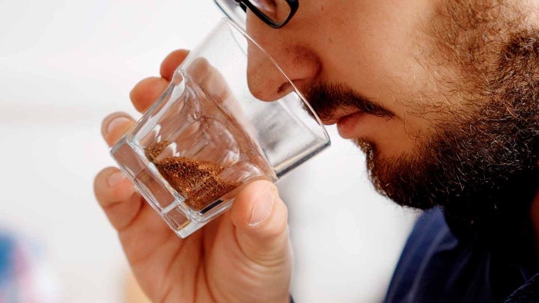 Hombre huele el café molido en una copa de cristal que sostiene con su mano frente a su rostro