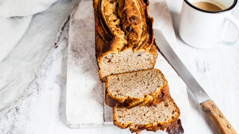 Pan de banano cortado en rebanadas, acompañado de una taza de café sobre fondo claro