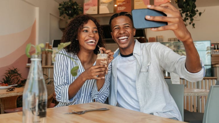 Una pareja sonriente se toma una selfie mientras disfruta una bebida en una cafetería moderna.