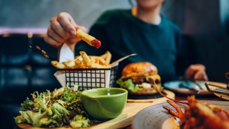 Persona disfrutando un menú casual con papas fritas, ensalada y hamburguesa en un restaurante.