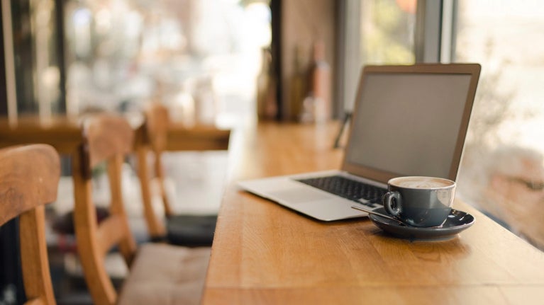 Café con laptop en barra de cafetería, ideal para analizar y ajustar precios de menú.