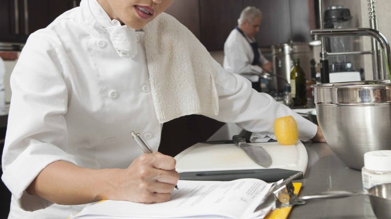 Chef revisa documentos en cocina profesional para identificar cuellos de botella en la operación. 